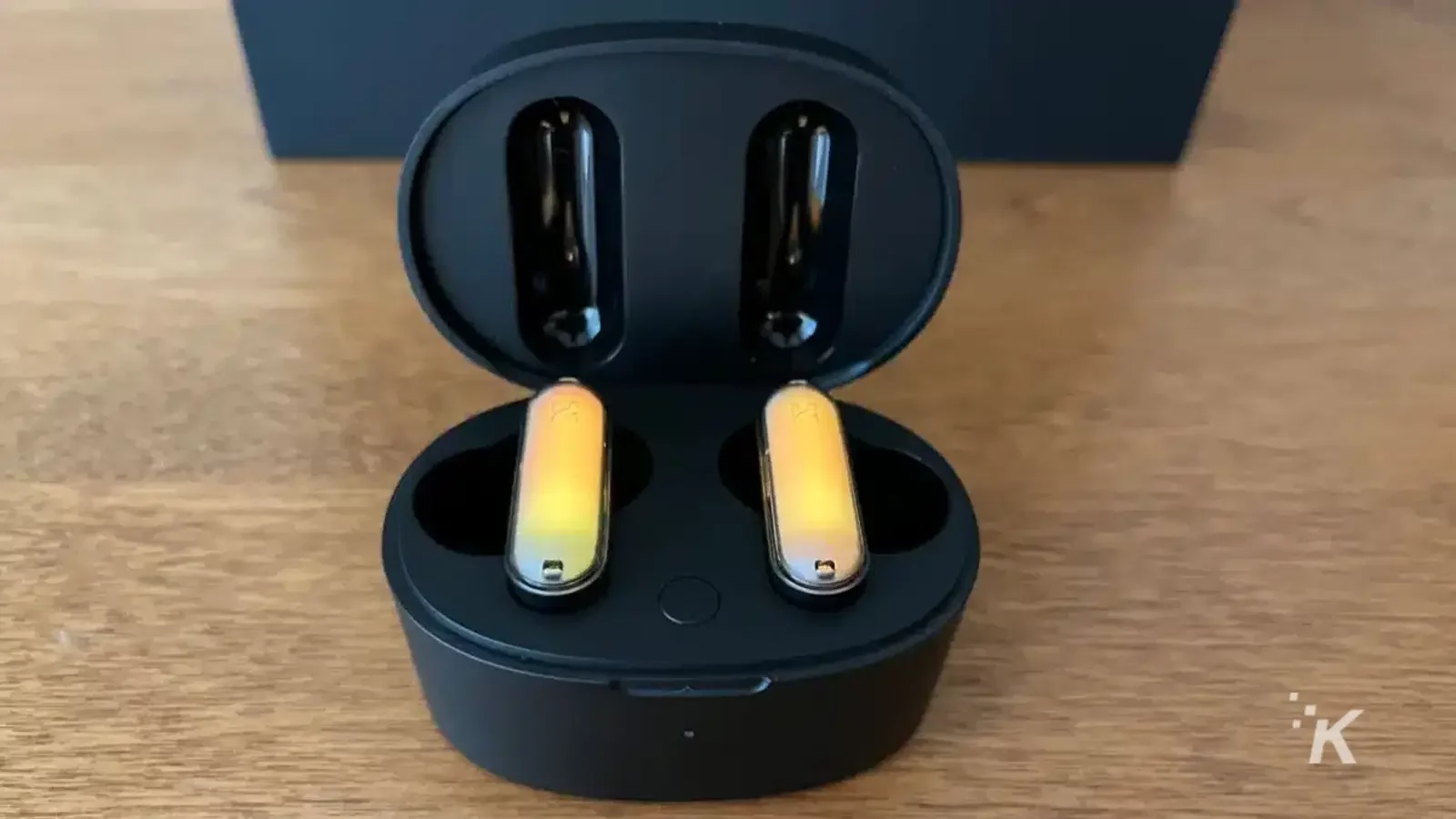 GPods earbuds in case on wooden table glowing yellow