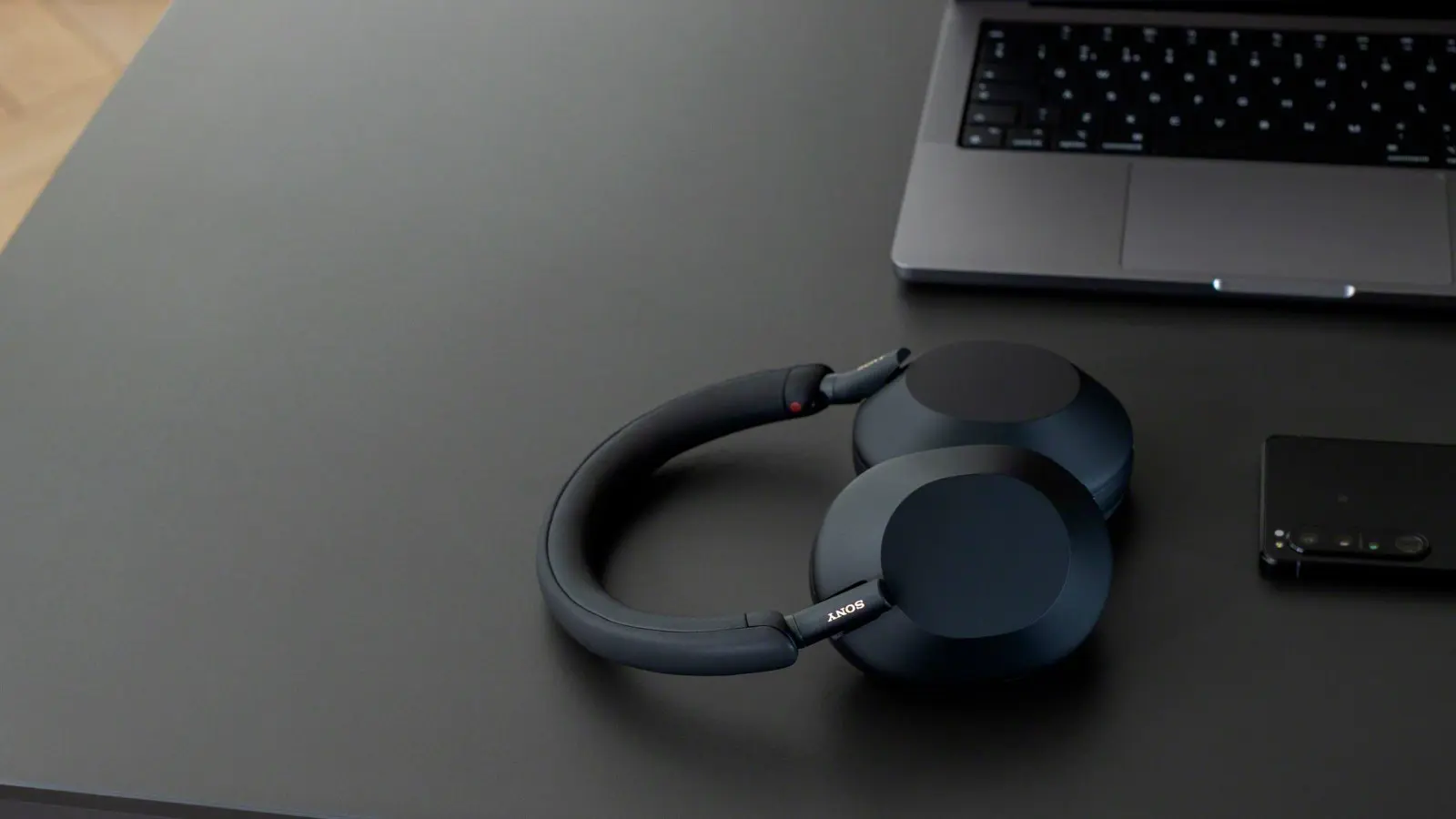 sony wh-1000xm5 headphones in black laid on a table near a laptop and phone